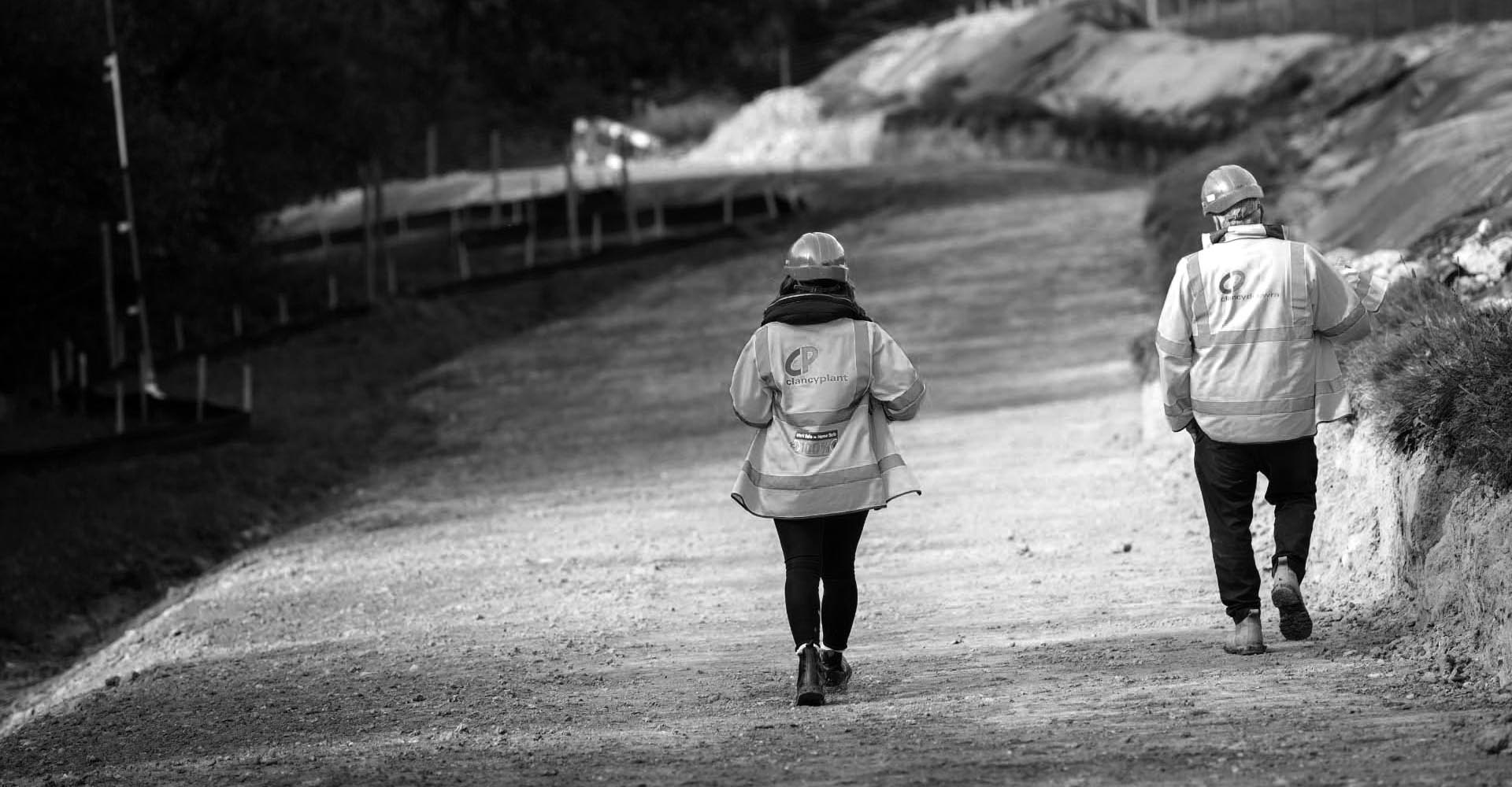 two people in hi-viz walking on a dirt road